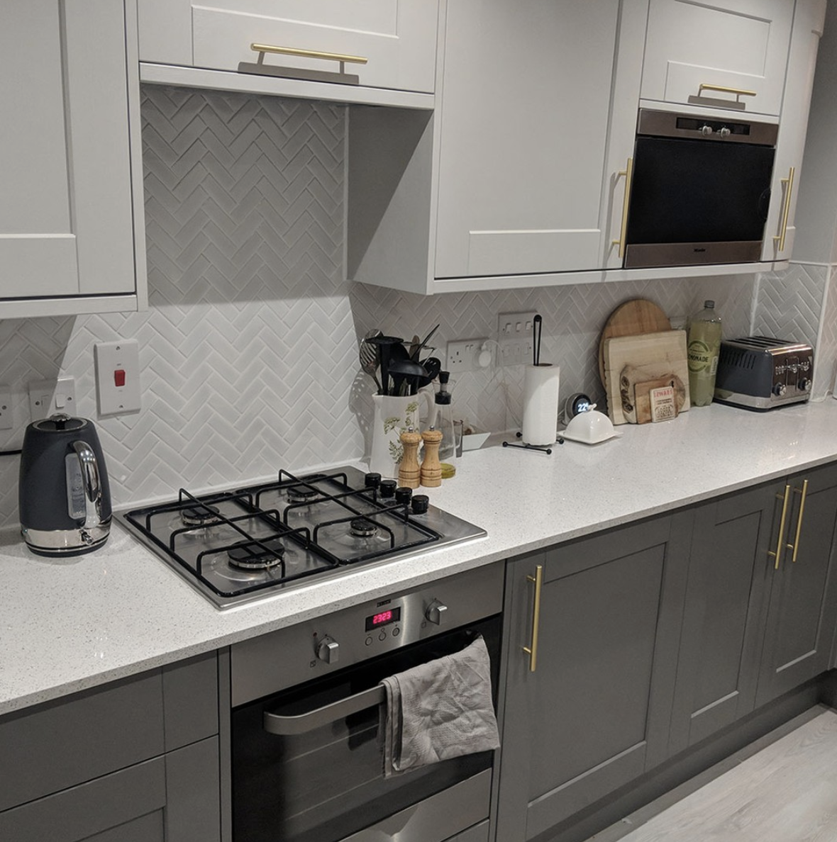 Gold Hardware and Matching Cabinets With a Grey Double Herringbone Backsplash